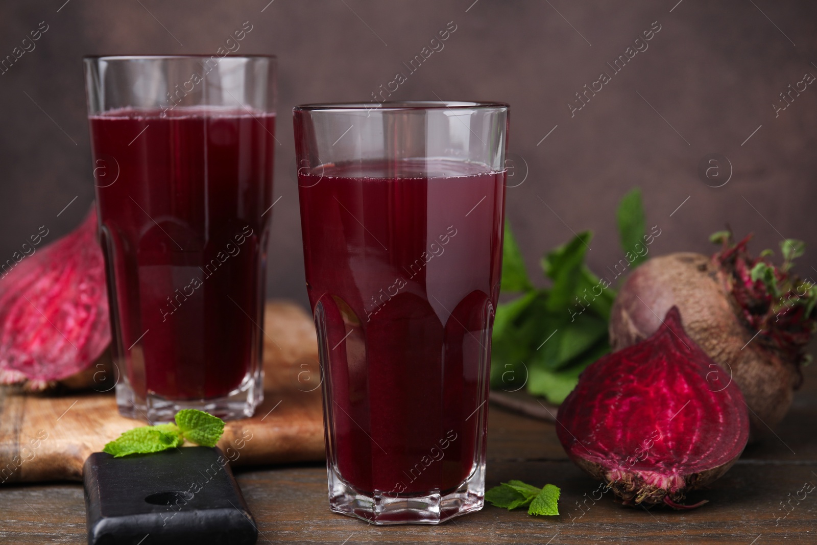 Photo of Fresh beet juice in glasses, ripe vegetables and mint on wooden table, closeup