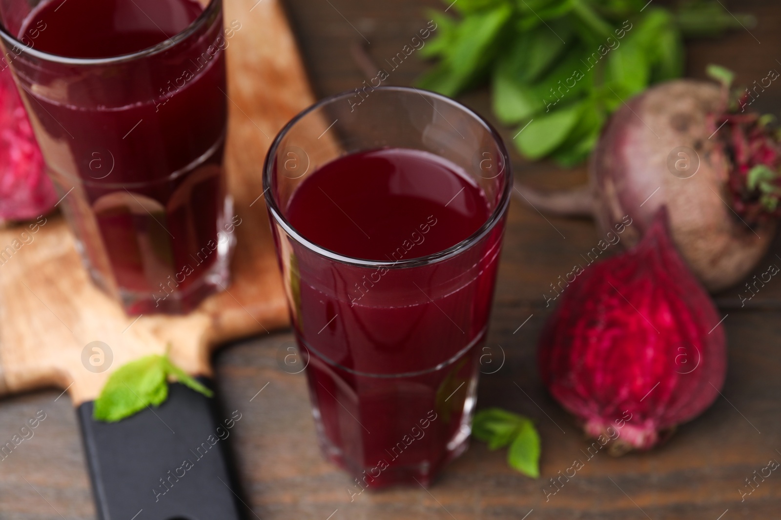 Photo of Fresh beet juice in glasses, ripe vegetables and mint on wooden table, closeup