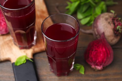 Fresh beet juice in glasses, ripe vegetables and mint on wooden table, closeup