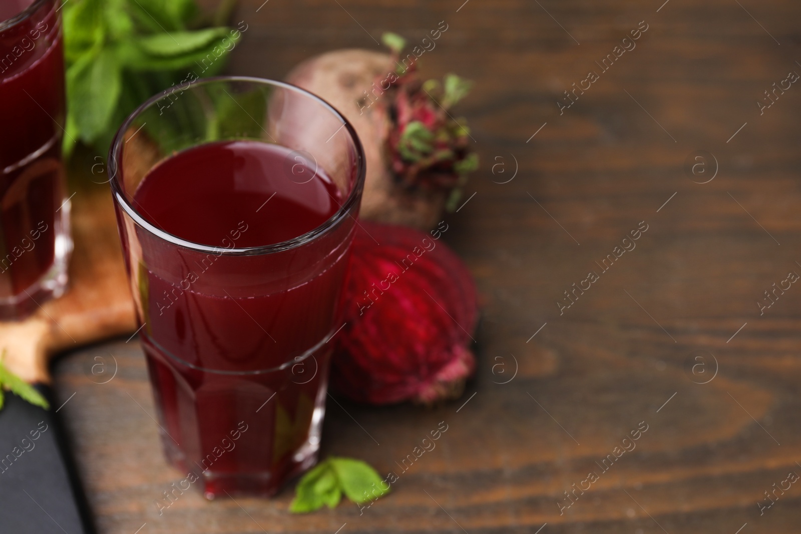 Photo of Fresh beet juice in glass and ripe vegetables on wooden table, closeup. Space for text