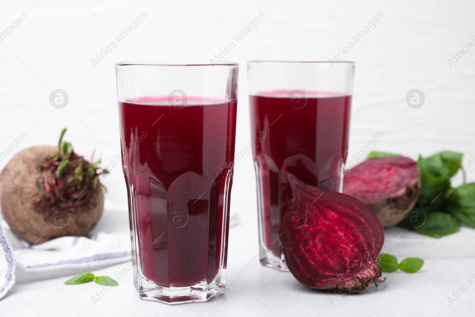 Photo of Fresh beet juice in glasses and ripe vegetables on light table, closeup