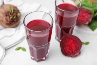 Photo of Fresh beet juice in glasses and ripe vegetables on light table, closeup