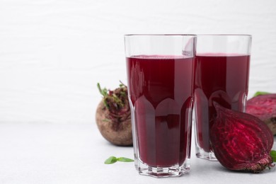 Fresh beet juice in glasses and ripe vegetables on white table, space for text