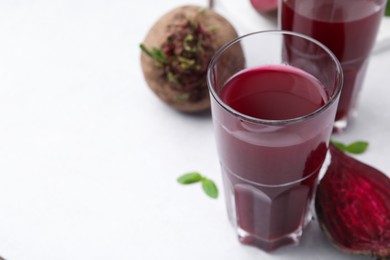 Photo of Fresh beet juice in glasses and ripe vegetables on white table, closeup. Space for text