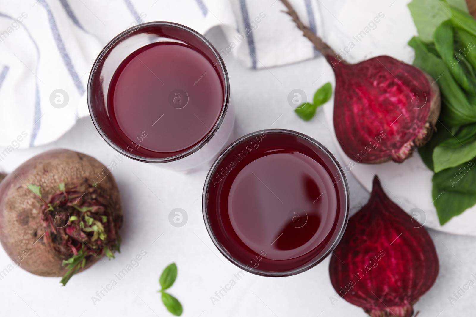 Photo of Fresh beet juice in glasses, ripe vegetables and basil on light table, flat lay