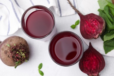 Photo of Fresh beet juice in glasses, ripe vegetables and basil on light table, flat lay