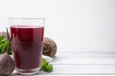 Photo of Fresh beet juice in glass, ripe vegetables and mint on white wooden table, space for text