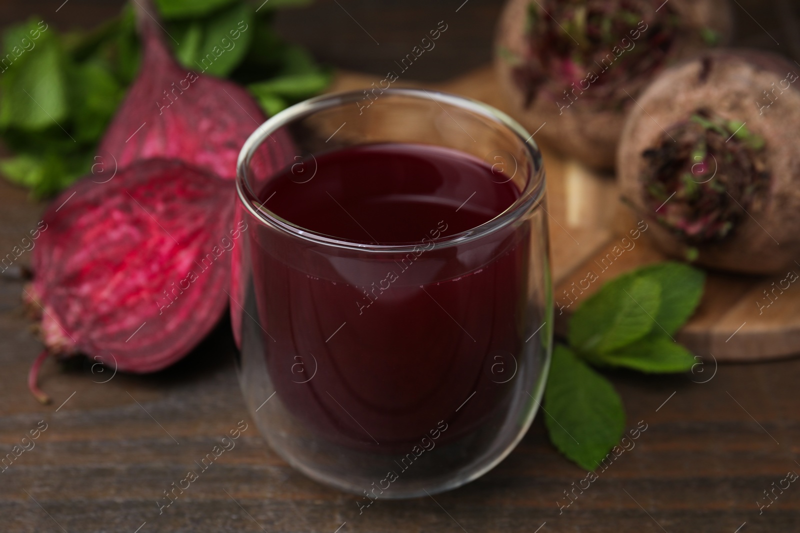 Photo of Fresh beet juice in glass, ripe vegetables and mint on wooden table, closeup