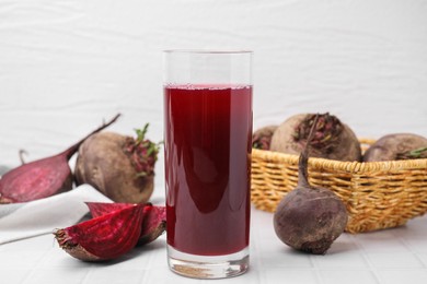 Fresh beet juice in glass and ripe vegetables on white tiled table