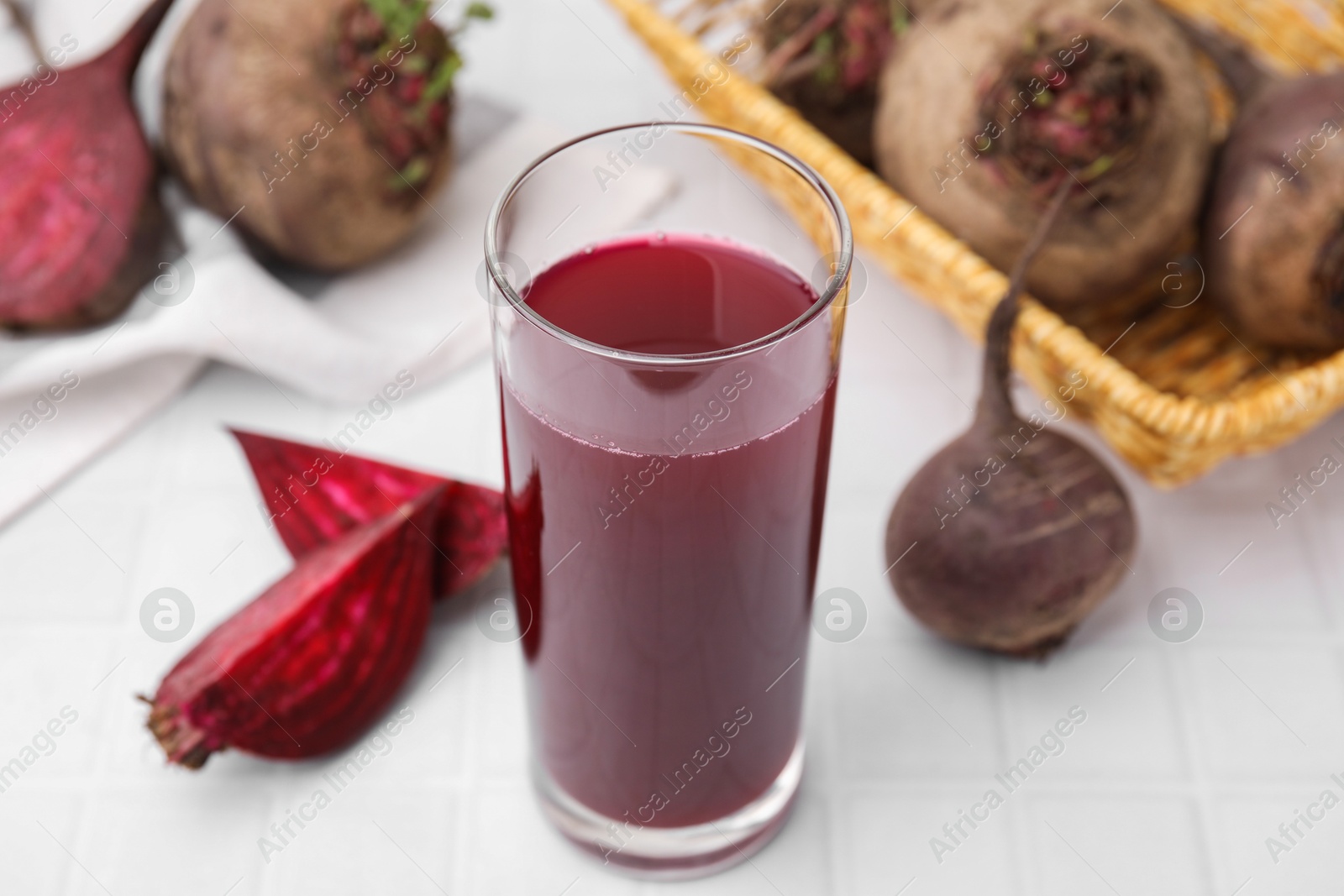 Photo of Fresh beet juice in glass and ripe vegetables on white tiled table, closeup