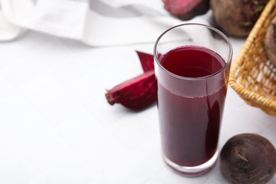 Photo of Fresh beet juice in glass and ripe vegetables on white tiled table, closeup. Space for text