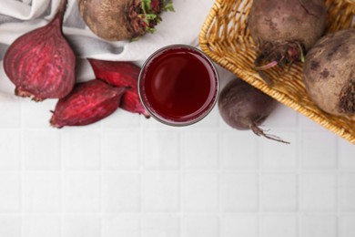 Photo of Fresh beet juice in glass and ripe vegetables on white tiled table, flat lay. Space for text