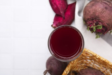 Photo of Fresh beet juice in glass and ripe vegetables on white tiled table, flat lay. Space for text