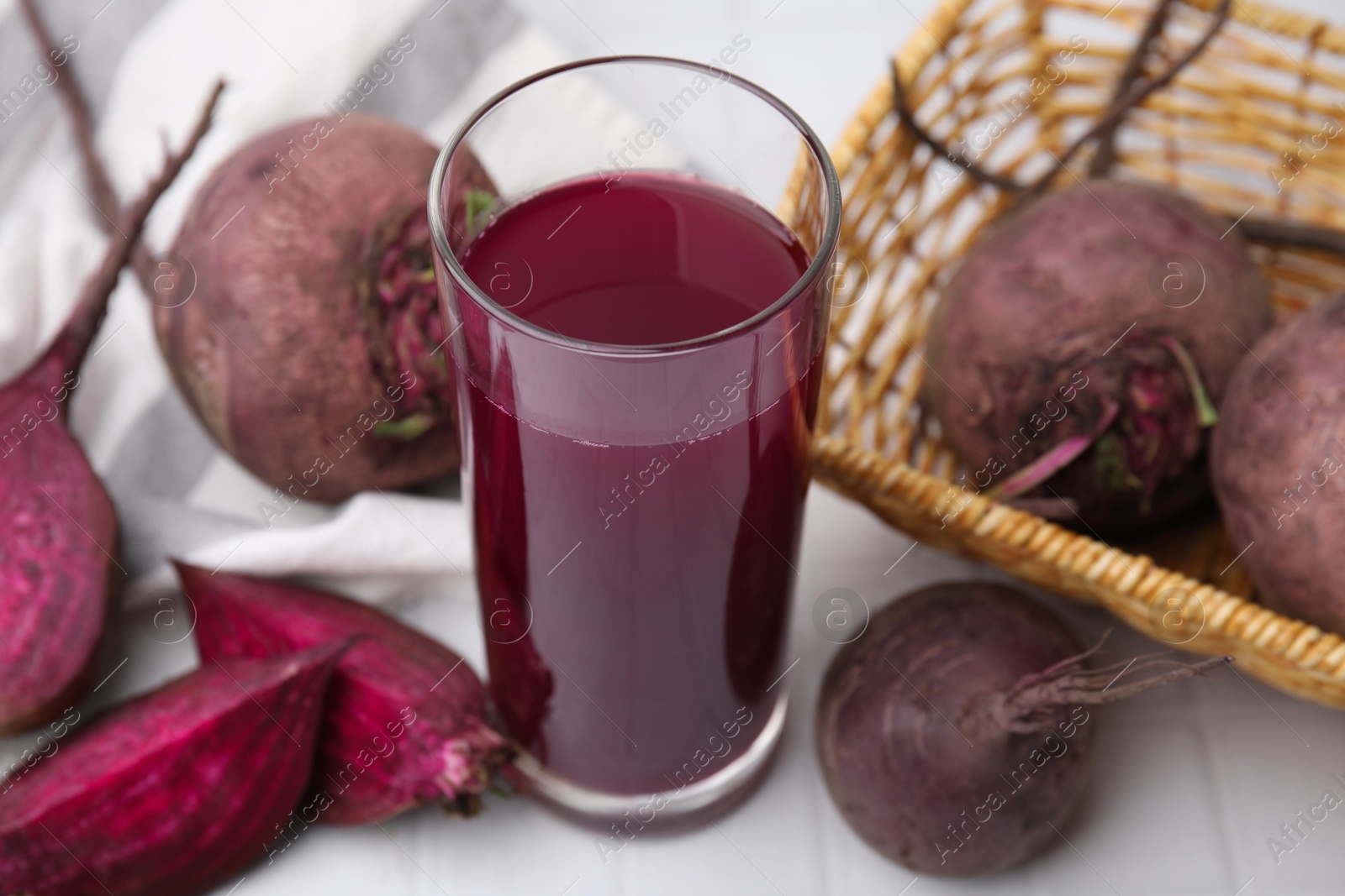 Photo of Fresh beet juice in glass and ripe vegetables on white tiled table, closeup