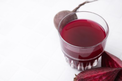 Photo of Fresh beet juice in glass and ripe vegetables on white tiled table, closeup. Space for text