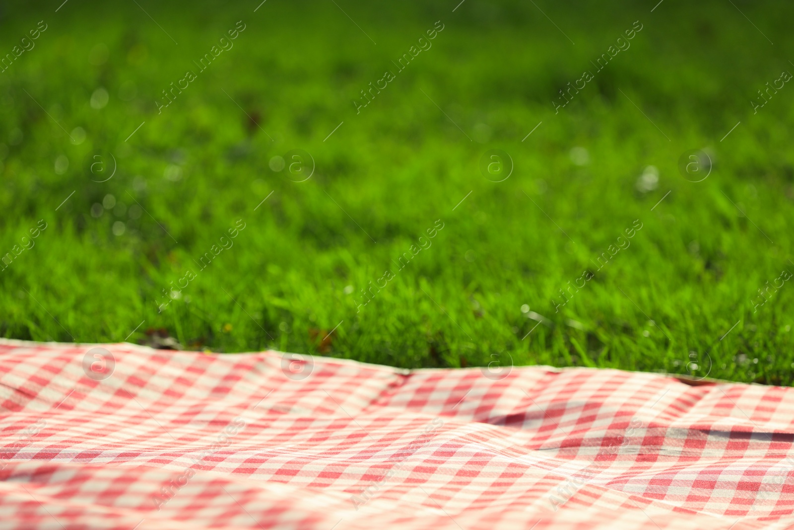 Photo of Checkered picnic tablecloth on green grass, closeup. Space for text