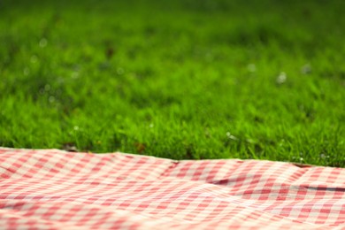 Photo of Checkered picnic tablecloth on green grass, closeup. Space for text