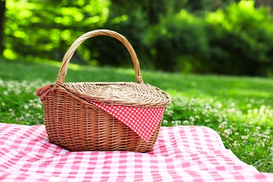 Photo of One picnic wicker basket with checkered napkin and blanket on green grass. Space for text