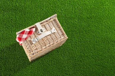 Photo of One picnic wicker basket with checkered napkin on green grass, above view. Space for text