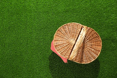 Photo of One picnic wicker basket with checkered napkin on green grass, top view. Space for text