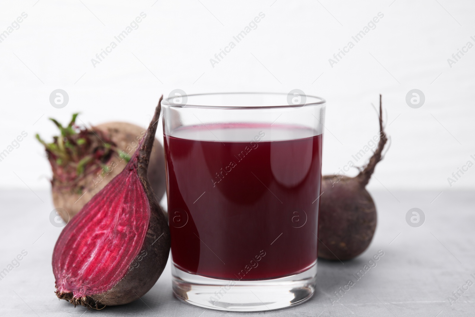 Photo of Fresh beet juice in glass and ripe vegetables on gray table against white background