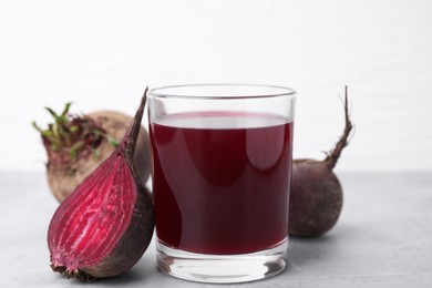 Photo of Fresh beet juice in glass and ripe vegetables on gray table against white background