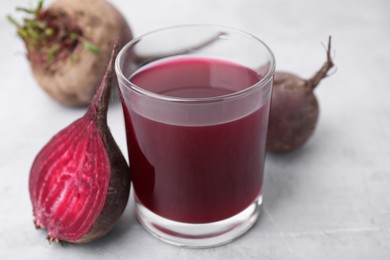 Photo of Fresh beet juice in glass and ripe vegetables on gray table, closeup