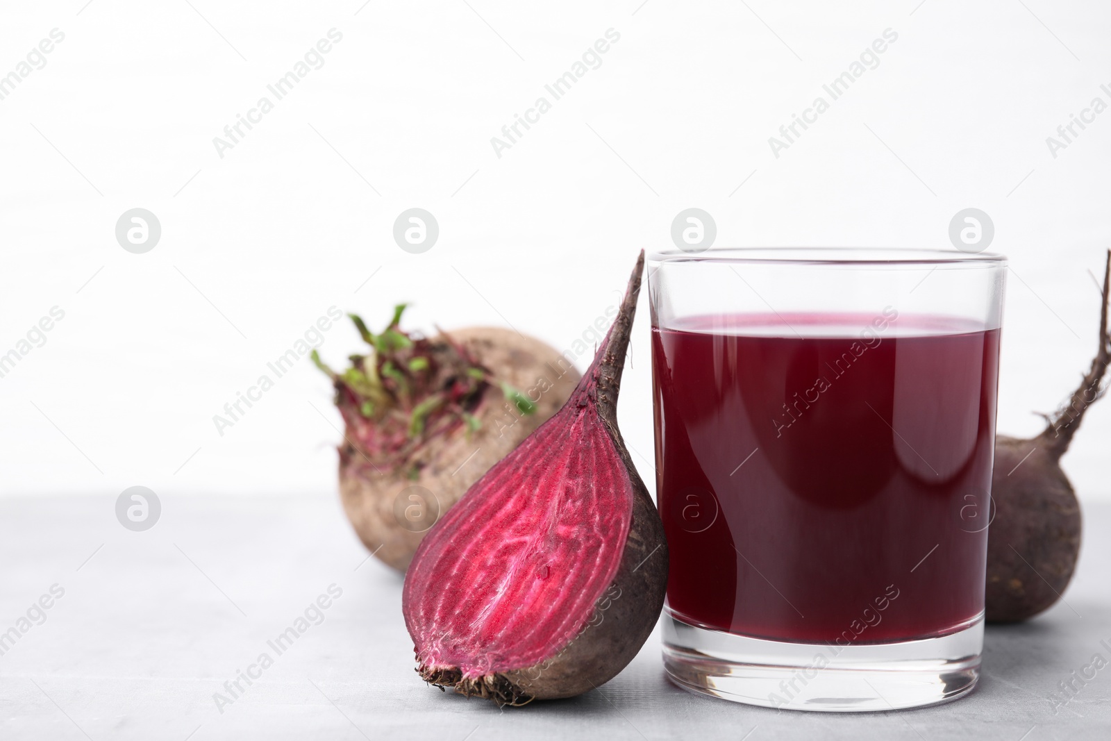 Photo of Fresh beet juice in glass and ripe vegetables on gray table against white background