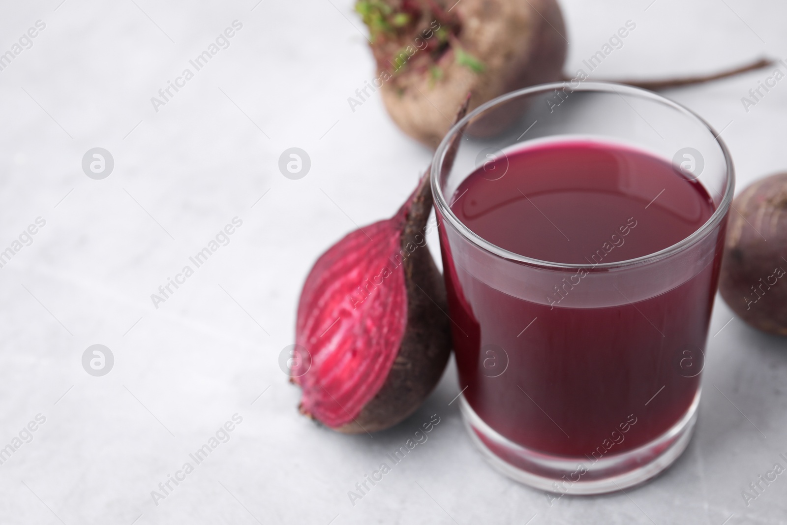 Photo of Fresh beet juice in glass and ripe vegetables on gray table, closeup. Space for text