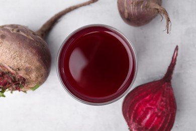 Photo of Fresh beet juice in glass and ripe vegetables on gray table, flat lay