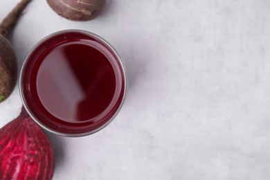 Photo of Fresh beet juice in glass and ripe vegetables on gray table, flat lay. Space for text