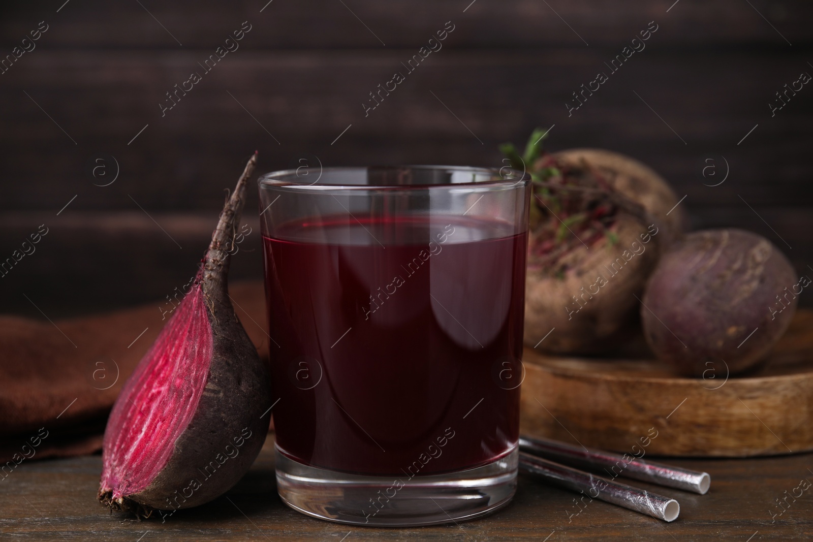 Photo of Fresh beet juice in glass, ripe vegetable and straws on wooden table, closeup