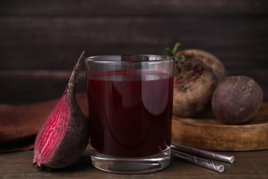 Photo of Fresh beet juice in glass, ripe vegetable and straws on wooden table, closeup