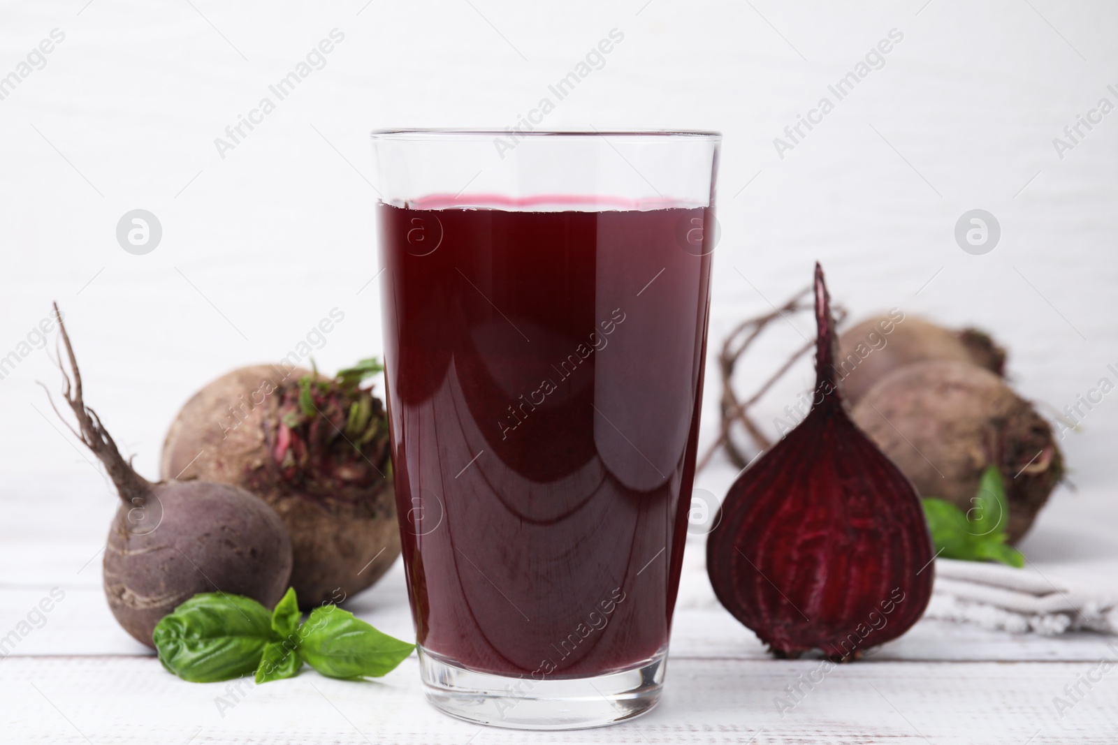 Photo of Fresh beet juice in glass, ripe vegetables and basil on light wooden table, closeup