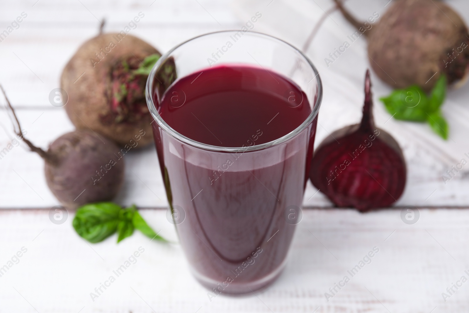 Photo of Fresh beet juice in glass and ripe vegetables on light wooden table, closeup