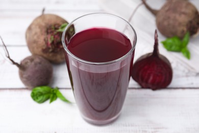 Photo of Fresh beet juice in glass and ripe vegetables on light wooden table, closeup