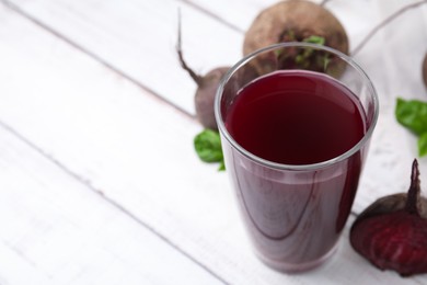 Photo of Fresh beet juice in glass and ripe vegetables on light wooden table, closeup. Space for text