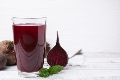 Photo of Fresh beet juice in glass, ripe vegetables and basil on light wooden table, space for text