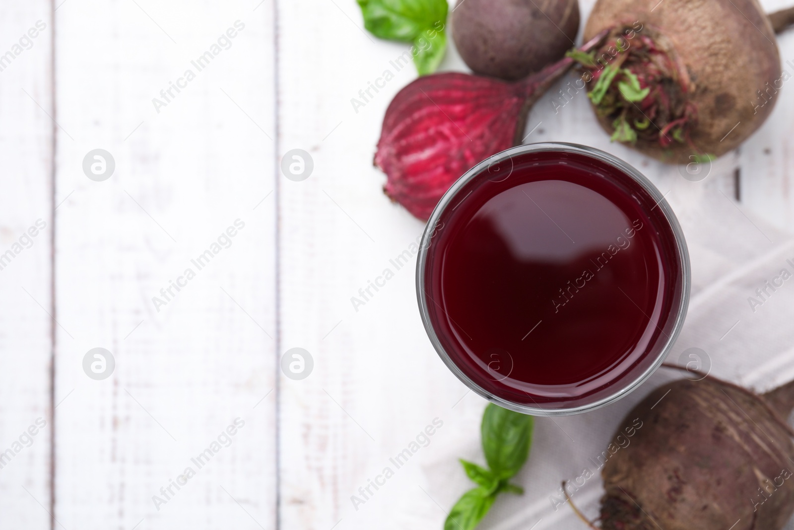 Photo of Fresh beet juice in glass, ripe vegetables and basil on light wooden table, flat lay. Space for text