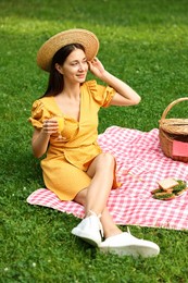 Smiling woman with glass of juice having picnic on green grass