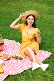 Smiling woman with glass of juice having picnic on green grass