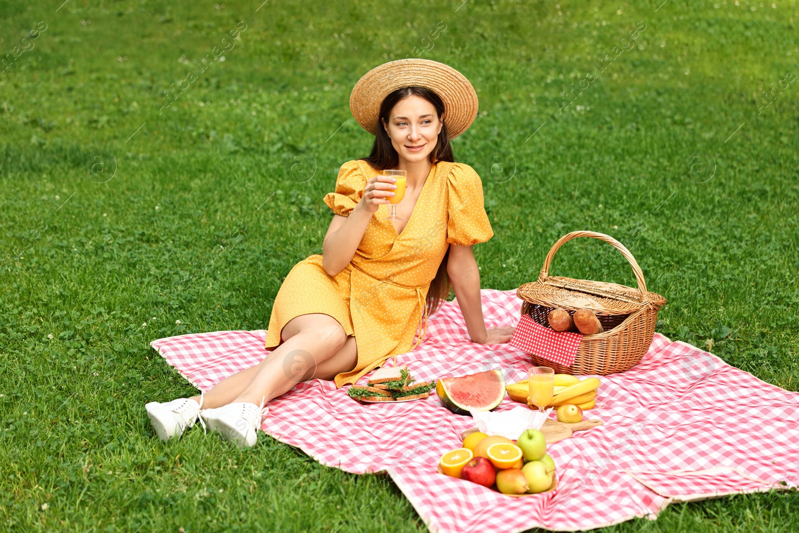 Photo of Beautiful woman with glass of juice having picnic on green grass