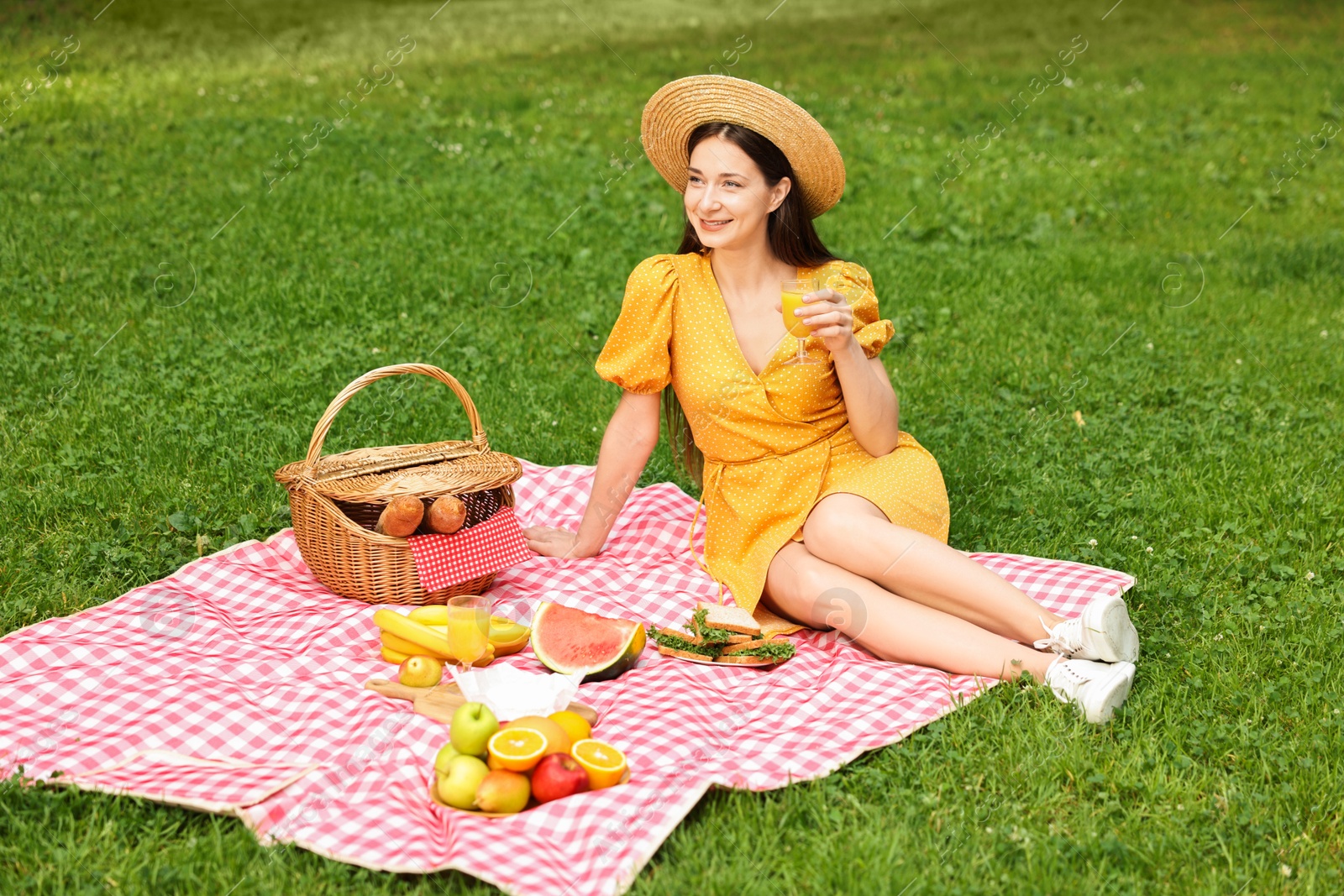 Photo of Smiling woman with glass of juice having picnic on green grass