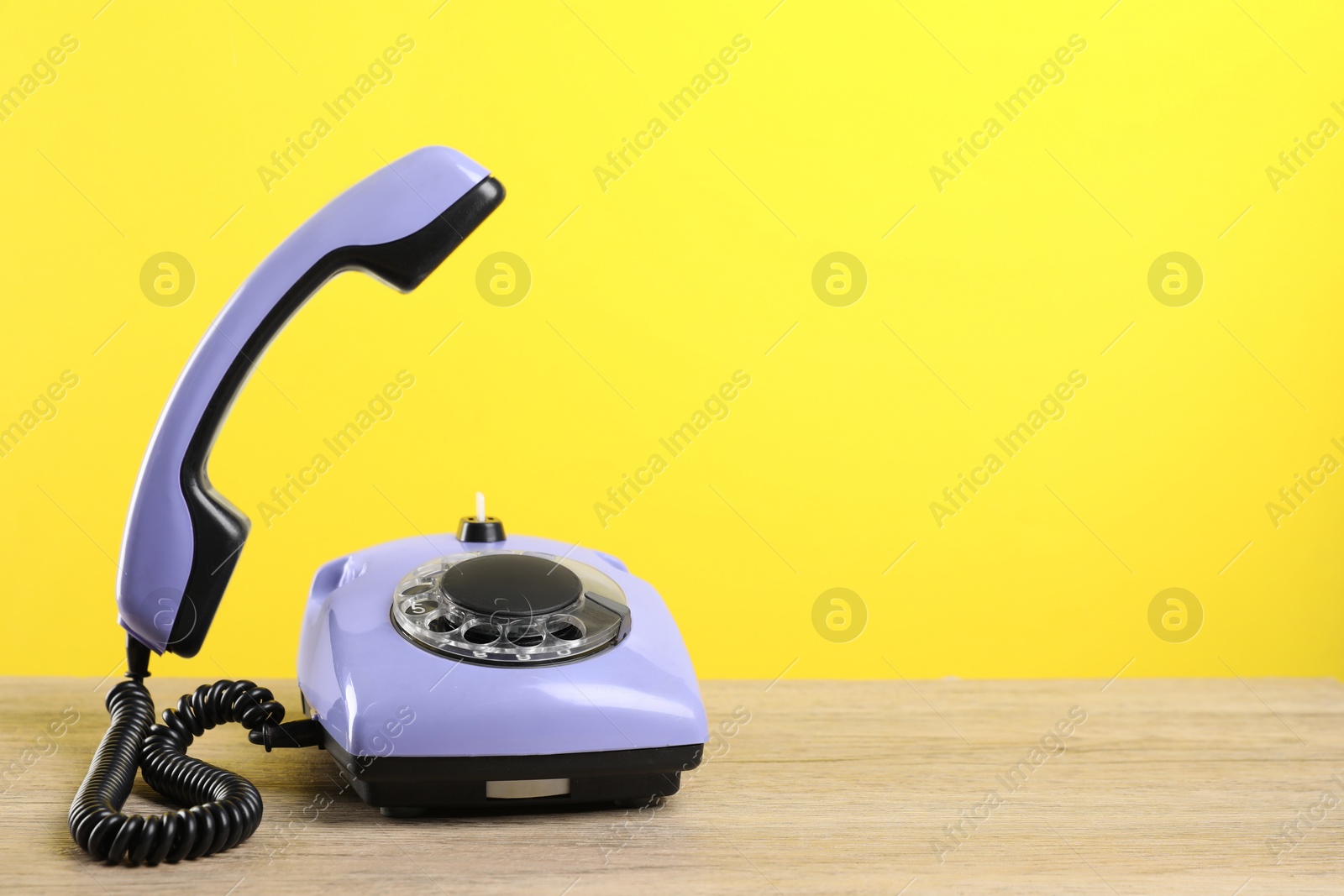 Photo of Violet telephone with handset on wooden table against yellow background, space for text