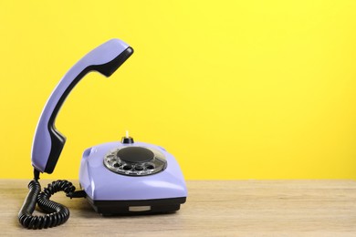 Photo of Violet telephone with handset on wooden table against yellow background, space for text