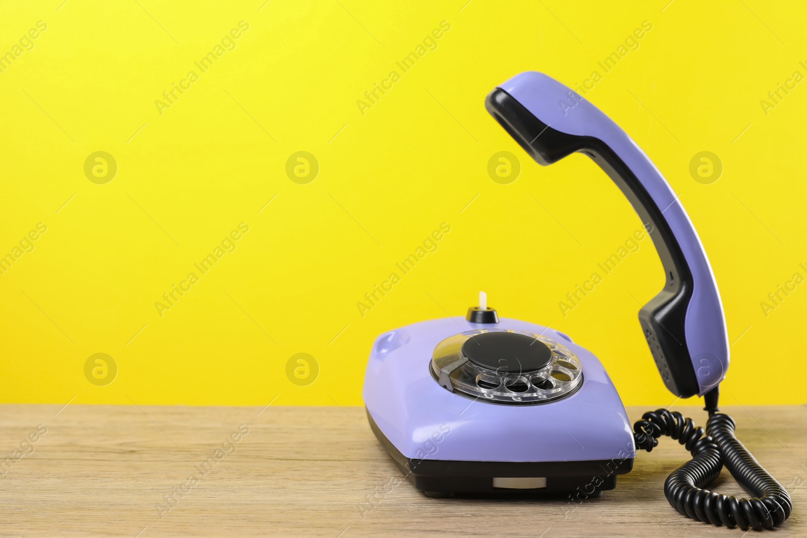 Photo of Violet telephone with handset on wooden table against yellow background, space for text