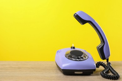 Violet telephone with handset on wooden table against yellow background, space for text