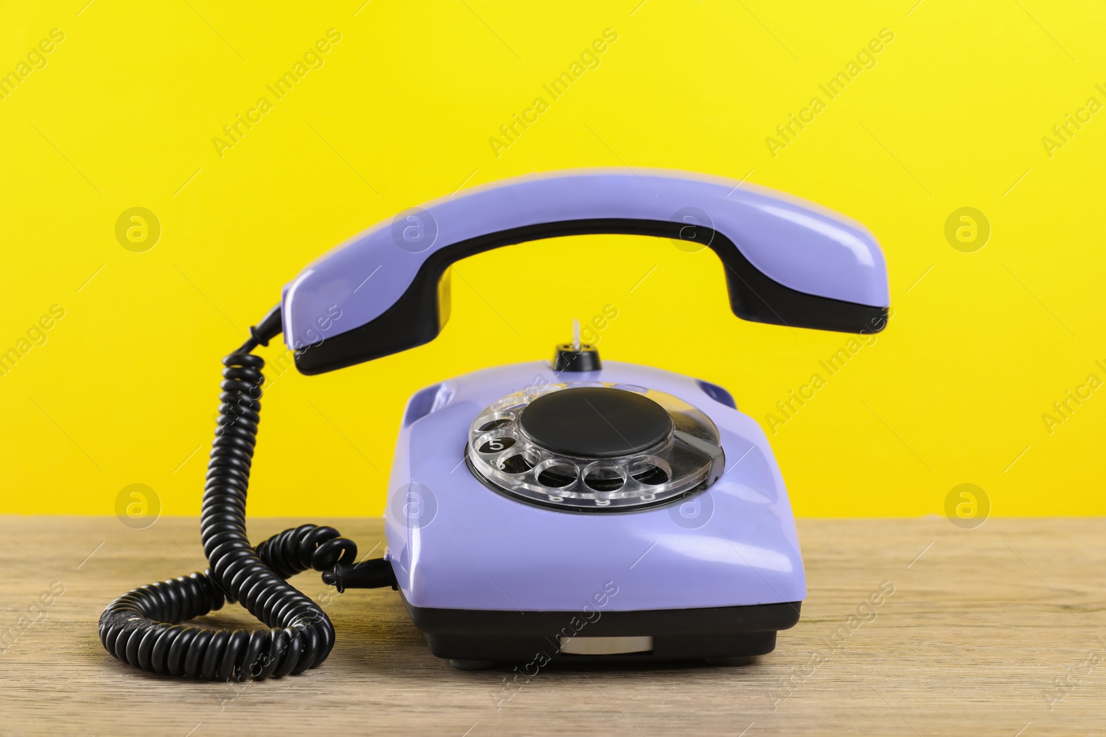 Photo of One violet telephone with handset on wooden table against yellow background