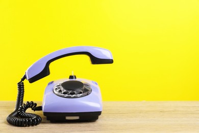 Photo of Violet telephone with handset on wooden table against yellow background, space for text