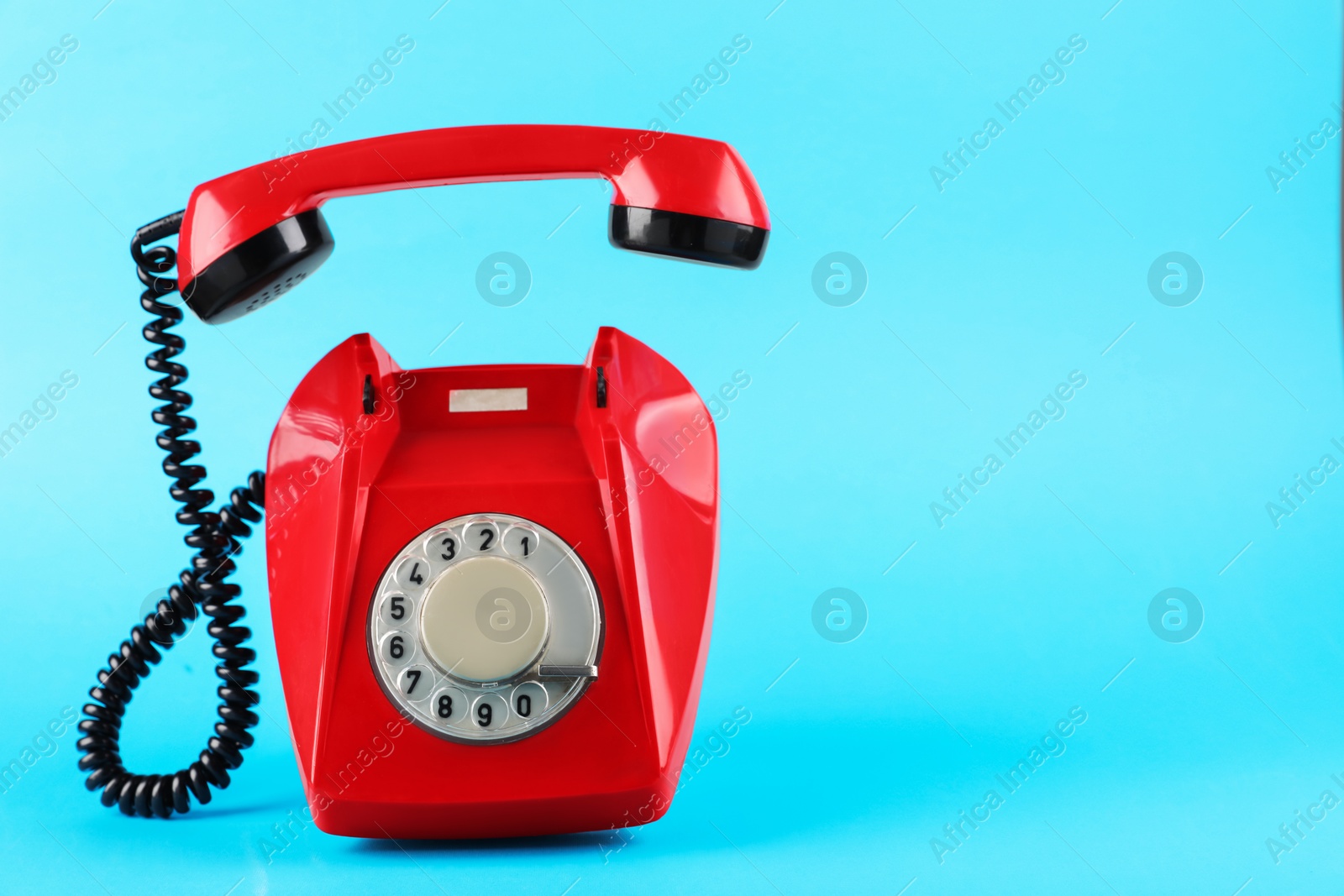 Photo of Red telephone with handset on light blue background, space for text